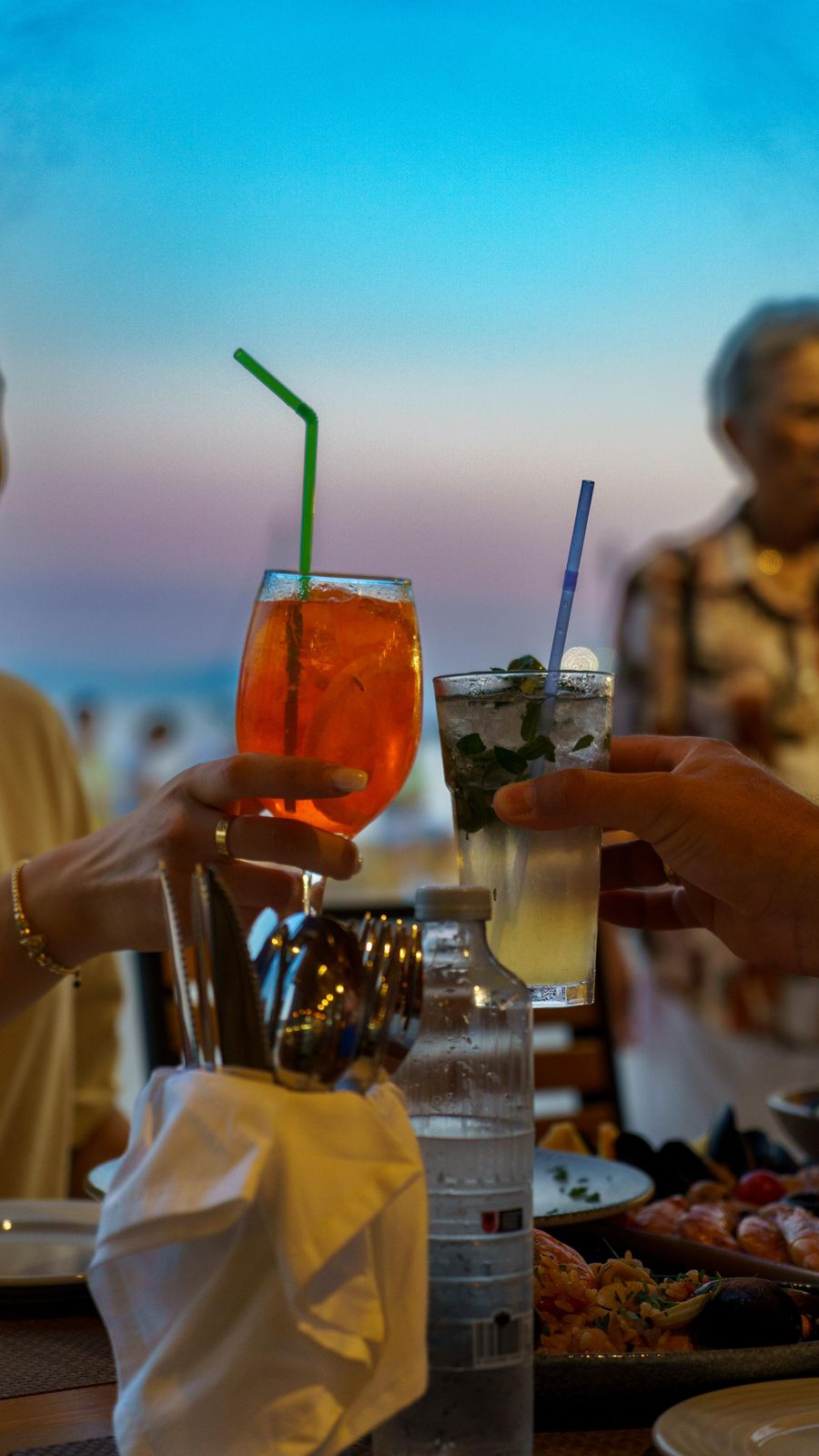 Spritz and mojito cheers against a dusk sky
