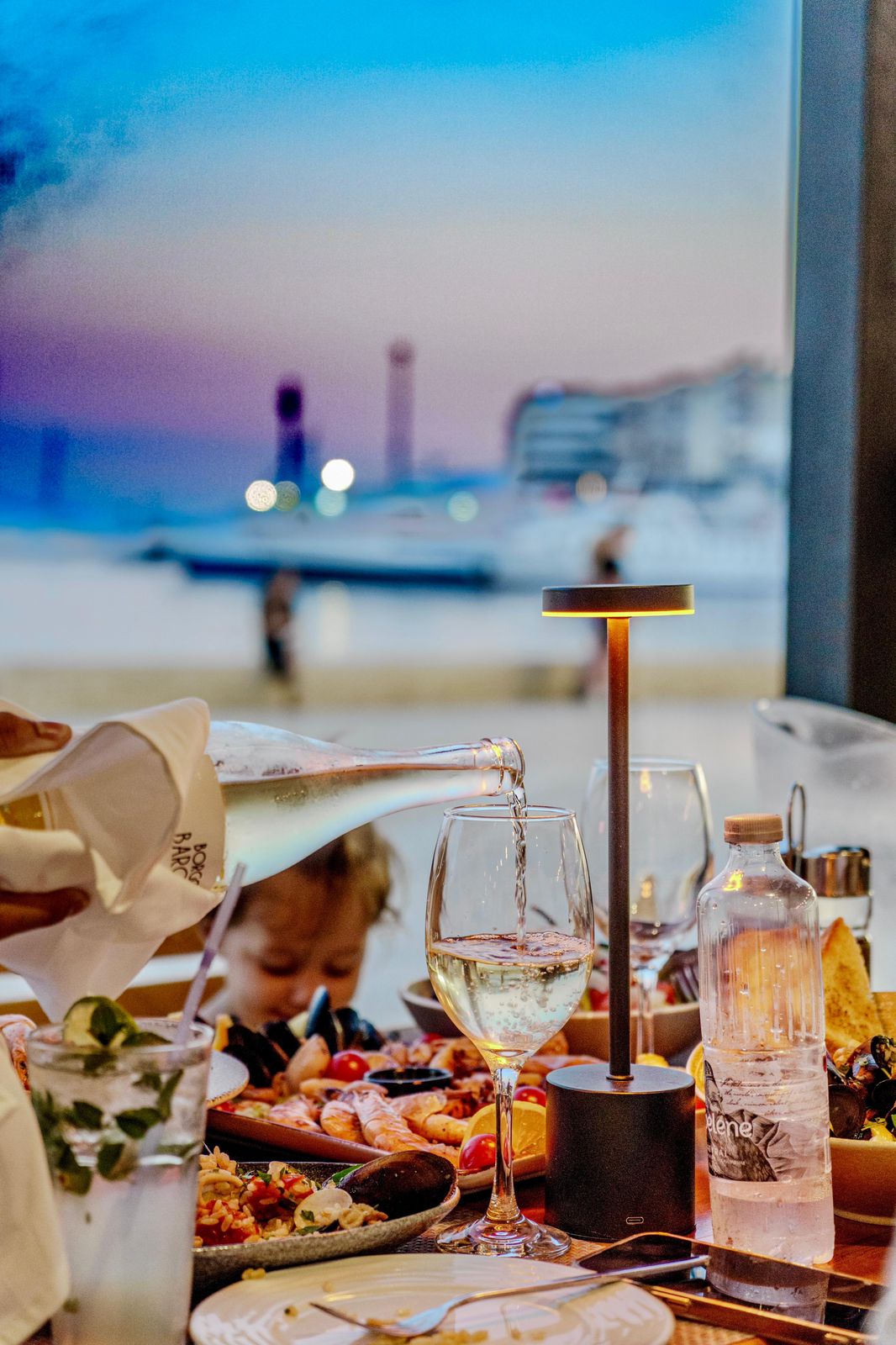 White wine poured tableside with harbor lights beyond